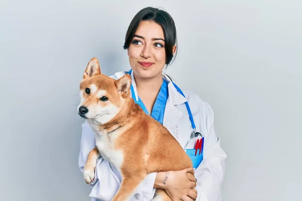 Beautiful Hispanic Veterinarian Woman Holding Dog Smiling Looking Side Staring — Stok fotoğraf