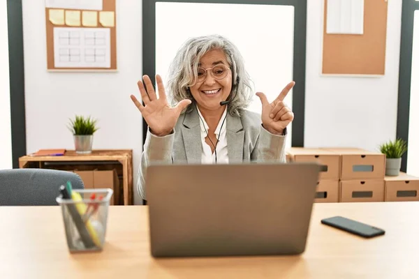 中年女商人坐在办公桌前 用笔记本电脑在办公室里展示 用七号手指指指 面带微笑 自信而快乐 — 图库照片