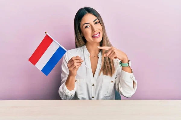 Jovem Hispânica Segurando Bandeira Holandesa Sentado Mesa Sorrindo Feliz Apontando — Fotografia de Stock