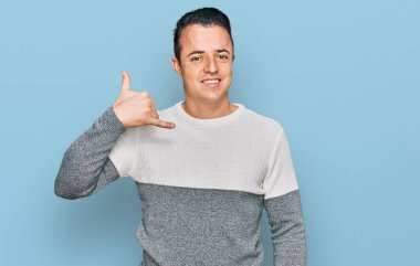 Handsome young man wearing casual winter sweater smiling doing phone gesture with hand and fingers like talking on the telephone. communicating concepts. 