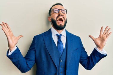 Sakallı, takım elbiseli ve kravatlı genç adam, başarı için çılgınca kutlama yapıyor. Kolları havada ve gözleri kapalı, heyecanla bağırıyor. Kazanan konsept 