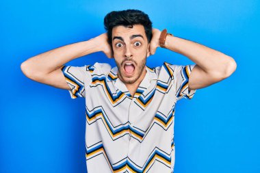 Gündelik kıyafetler giyen genç İspanyol adam çılgın ve elleri başında korkmuş, ağzı açık şoktan korkmuş ve şaşırmış. 