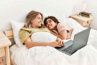 Genç çift yatak odasında dizüstü bilgisayar kullanarak film izliyor.