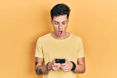 Genç İspanyol adam akıllı telefon kullanarak mesaj yazıyor. Korkmuş ve şok olmuş bir şekilde şaşkınlık, şaşkınlık ifadesi, korku ve heyecan dolu bir yüz.. 