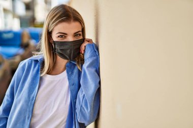 Koronavirüs maskesi takan genç sarışın kız şehirde dikiliyor..