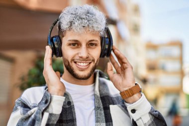 Şehirde kulaklık takarak mutlu gülümseyen genç İspanyol adam..