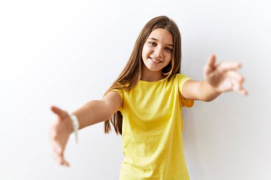 Genç esmer ergen, izole edilmiş arka planda yan yana durmuş kameraya bakarak sarılmak için kollarını açmış gülümsüyor. Mutluluğu kucaklayan neşeli bir ifade.. 
