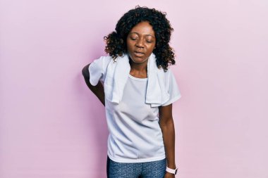 Young african american woman wearing sportswear and towel suffering of backache, touching back with hand, muscular pain 