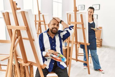 Sanat atölyesinde kıdemli bir sanatçı gülümseyerek saçlara dokunarak, el hareketi yaparak, çekici ve modaya uygun bir şekilde poz verir. 