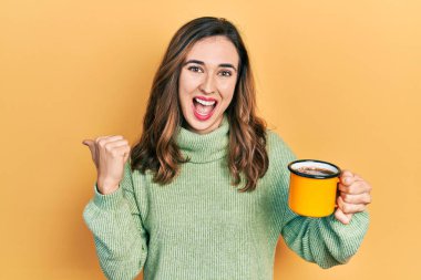 Genç İspanyol kız bir fincan kahve içiyor başparmağıyla yan tarafa bakıyor mutlu bir şekilde gülümsüyor ve ağzı açık. 