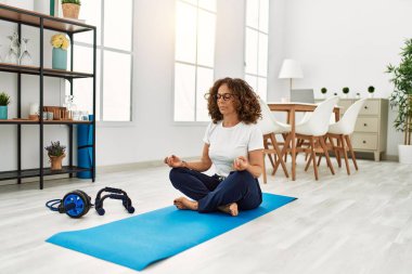 Olgun İspanyol kadın evdeki oturma odasında yoga meditasyonu yapıyor.