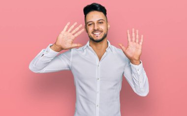 Genç Arap adam gündelik giysiler giyer ve parmaklarını on numarayla gösterir ve gösterirken kendinden emin ve mutlu gülümserdi.. 
