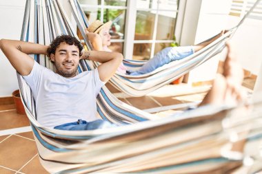 Mutlu gülümseyen genç çift, elleri başlarının üzerinde terasta uzanmış bir şekilde rahatlar..