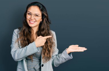 İş kıyafetleri ve gözlük takan genç İspanyol kız kameraya hayret ediyor ve gülümsüyor.. 