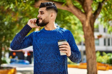 Genç Arap adam akıllı telefondan konuşuyor parkta kahve içiyor.