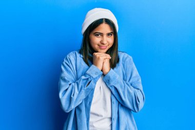 Tatlı yün şapkalı genç Latin kadın gergin ve heyecanlı bir şekilde çene kenarına bakıyor. 