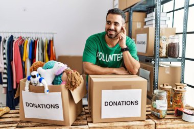 Hayır kurumunda bağış kutusuna yaslanmış gönüllü üniforması giyen İspanyol bir genç.