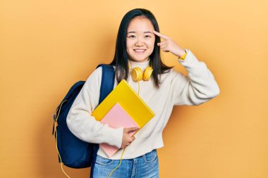 Sırt çantası tutan genç Çinli kız ve tek parmakla gülümseyen kitaplar, harika bir fikir ya da düşünce, iyi bir hafıza. 
