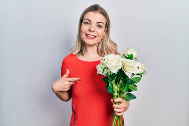 Beyaz çiçek buketi tutan güzel beyaz kadın mutlu bir şekilde elini ve parmağını gösterdi. 