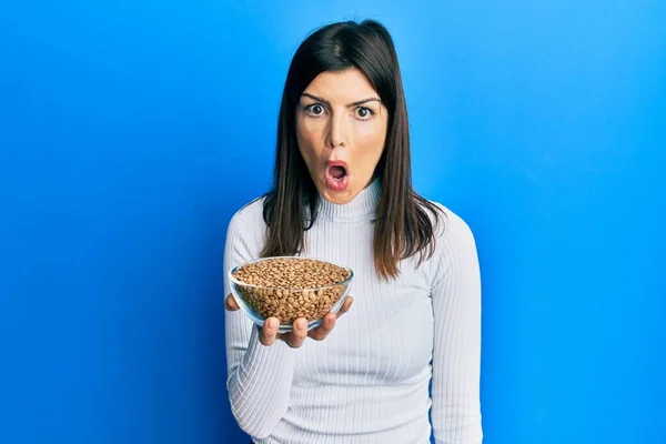 Young Hispanic Woman Holding Lentils Bowl Scared Amazed Open Mouth — стоковое фото