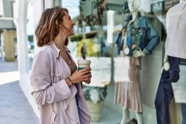 年轻的高加索女孩在城里喝咖啡 看服装店的橱窗 — 图库照片