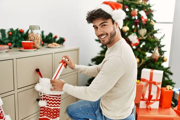 Ung Latinamerikansk Man Ler Glad Bär Jul Hatt Hålla Gåva — Stockfoto