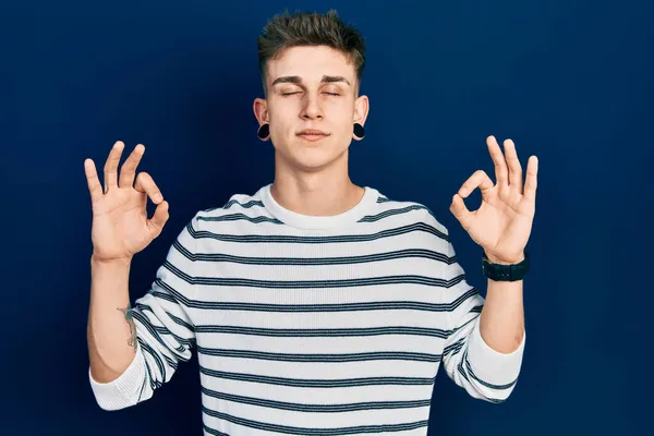 カジュアルなストライプのシャツを着て耳の拡張を持つ若い白人の少年は 指で瞑想のジェスチャーを行う閉じて目でリラックスして笑顔 ヨガのコンセプト — ストック写真