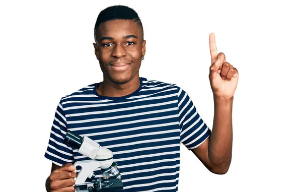 Joven Hombre Afroamericano Sosteniendo Microscopio Sonriendo Con Una Idea Pregunta —  Fotos de Stock