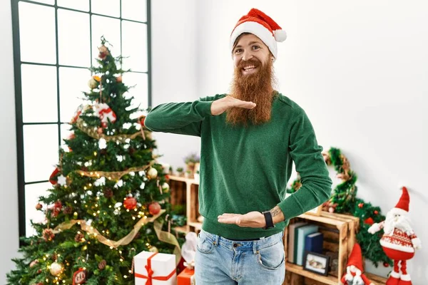 红头发的男人 留着长胡子 头戴圣诞帽 手拿着大号和大号标志 象征着圣诞节的到来 微笑着看着摄像机 计量概念 — 图库照片