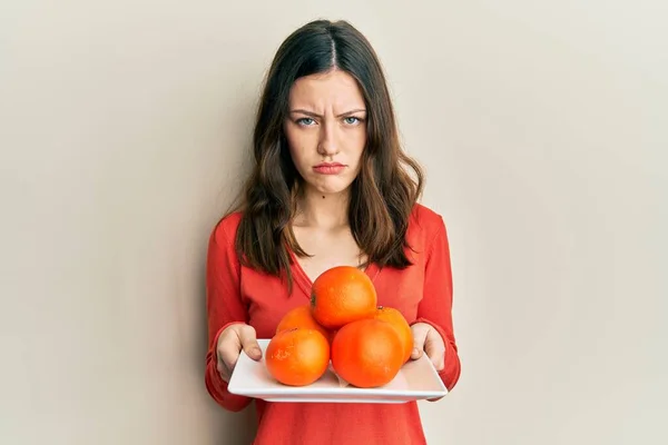 Νεαρή Μελαχρινή Γυναίκα Κρατώντας Πιάτο Φρέσκα Πορτοκάλια Κατάθλιψη Και Ανησυχούν — Φωτογραφία Αρχείου