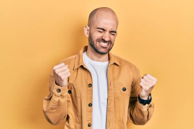 Genç kel bir adam, gündelik giysiler içinde çok mutlu ve heyecanlı bir şekilde kollarını kaldırıp, gülümseyerek ve başarı için çığlık atarak kazanan bir jest yapıyor. kutlama konsepti. 