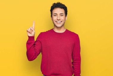 Gündelik kıyafetler giyen genç yakışıklı bir numarayı gösterip işaret ederken kendinden emin ve mutlu bir şekilde gülümsüyor.. 