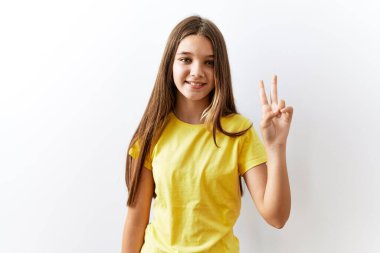 Genç esmer kız izole edilmiş arka planda yan yana duruyor. İki numaralı parmaklarıyla işaret ediyor ve gülümsüyor. Kendinden emin ve mutlu.. 