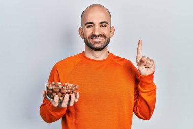 Elinde çiğ fındık tutan genç kel bir adam bir fikir veya soruyla gülümsüyor ve mutlu bir yüzle işaret ediyor. 