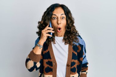 Orta yaşlı İspanyol bir kadın akıllı telefondan konuşuyor. Korkmuş ve ağzı açık bir şekilde şaşırmış, inançsız bir yüz ifadesi var. 