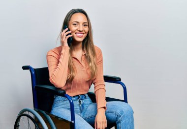 Tekerlekli sandalyede oturan güzel İspanyol kadın telefonda konuşurken mutlu ve pozitif görünüyor. Kendine güvenen bir gülümsemeyle dişlerini gösteriyor. 