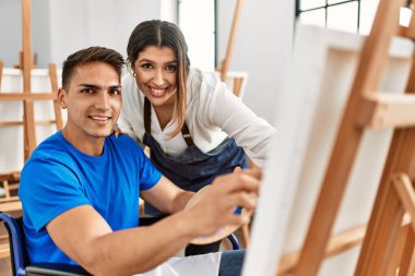 Öğretmen ve engelli boyacı. Tekerlekli sandalyede oturmuş resim yaparken gülümsüyor..