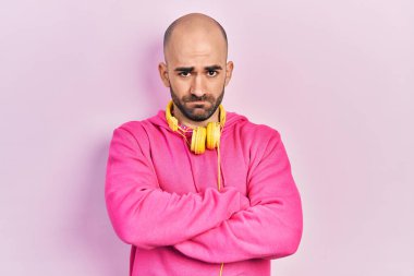 Spor kıyafetleri giyen, kulaklık takan kuşkucu ve gergin genç kel bir adam. Yüzünde çapraz kollu tasvip etmeyen bir ifade var. negatif kişi. 