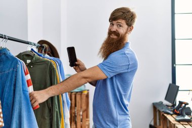 Genç kızıl saçlı müşteri elbise mağazasından kıyafet seçerken akıllı telefonuyla fotoğraf çekiyor..