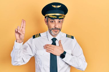 Handsome middle age man with grey hair wearing airplane pilot uniform smiling swearing with hand on chest and fingers up, making a loyalty promise oath 