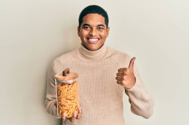 Genç, yakışıklı, elinde makarna dolu bir kavanoz tutan mutlu ve pozitif gülümseyen, başparmağıyla mükemmel ve onay işareti yapan bir İspanyol. 