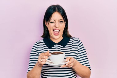 Bir fincan kahve içen genç İspanyol kadın kameraya seksi bir ifadeyle bakıyor, neşeli ve mutlu bir yüzle.. 