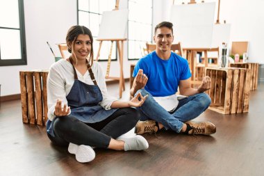 İki öğrenci, sanat okulunda yoga yaparken yerde otururken mutlu bir şekilde gülümsüyor..