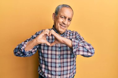 Gri saçlı, sıradan tişörtlü, aşık bir şekilde gülümseyen ve elleriyle kalp sembolü yapan yakışıklı bir son sınıf öğrencisiydi. romantik kavram. 