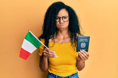 Orta yaşlı Afro-Amerikalı kadın elinde İtalyan bayrağı ve komik suratıyla yanaklarını şişiren pasaport tutuyor. Ağzı havayla şişer, havayı yakalar.. 