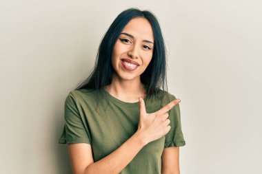 Gündelik tişörtler giyen genç İspanyol kız. Yüzünde mutlu ve doğal bir ifadeyle elleri ve parmaklarıyla yüzünü gösteren bir gülümseme. 