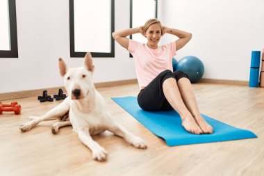 Genç beyaz kadın gülümsüyor spor merkezinde köpekle antreman yapıyor.