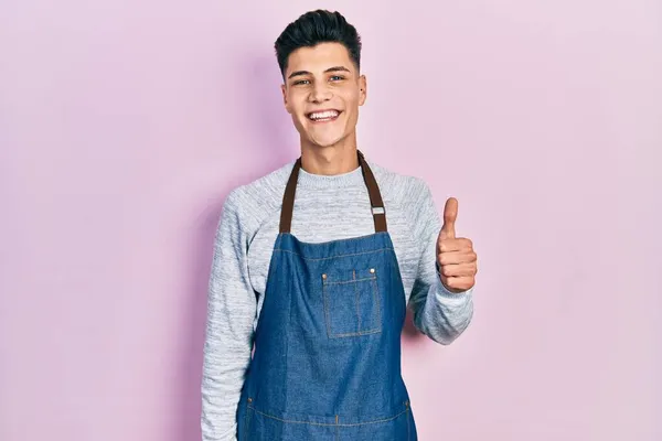 Önlük Giymiş Genç Spanyol Adam Mutlu Pozitif Gülümsüyor Başparmağıyla Mükemmel — Stok fotoğraf