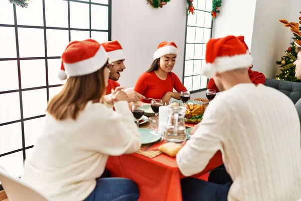 Bir grup genç, mutlu bir şekilde gülümseyerek evde Noel yemeği yiyor..