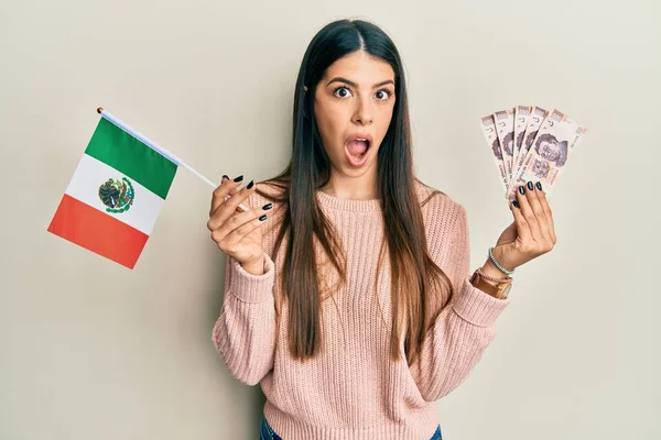 メキシコの国旗とメキシコのペソ紙幣を持っている若いヒスパニック系の女性は 驚きと驚きの表情 恐怖と興奮した顔で恐れとショックを受けました — ストック写真